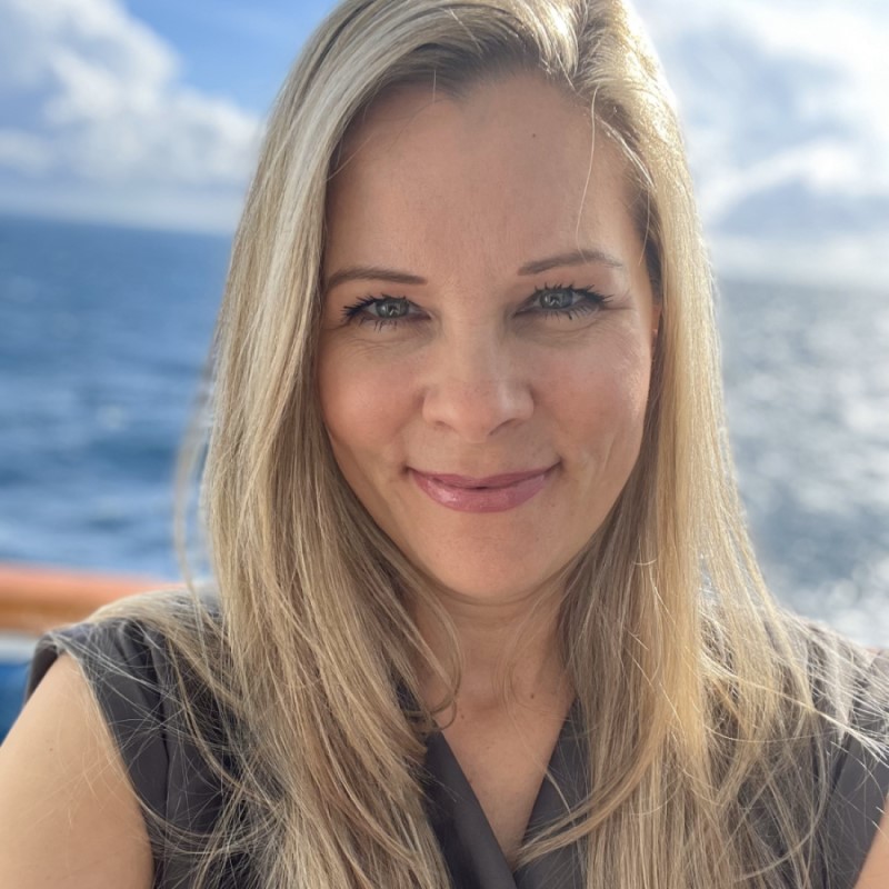 Image of Julie (Cruisinjules) standing on a cruise ship over-looking the ocean.