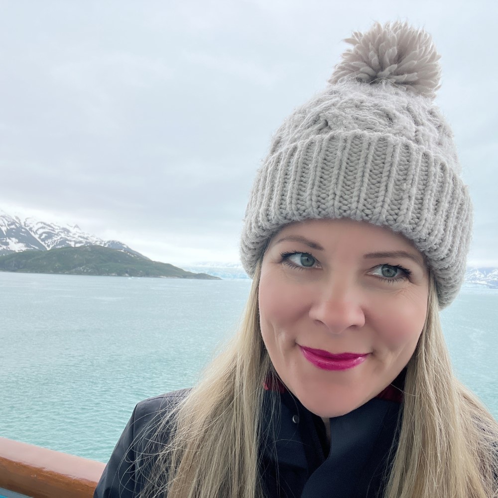 Picture of Julie (Cruisingjules) standing in front of an Alaskan shoreline.