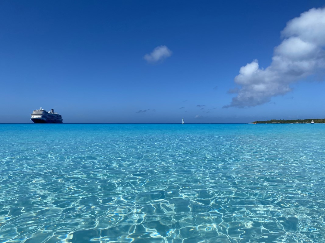 A beautiful landscape photo that displays the crystal clear ocean waters, with a cruise ship on the left hand side of the horrizon line.